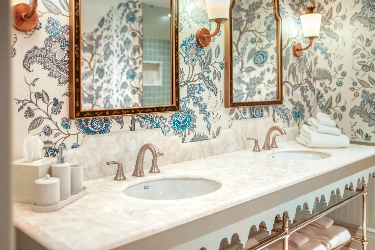 An elegant bathroom with double sinks, ornate mirrors, decorative wallpaper, and luxury lighting. The sophisticated design complements relaxation and self-care routines, inviting guests to indulge in organic bath products and pampering rituals.