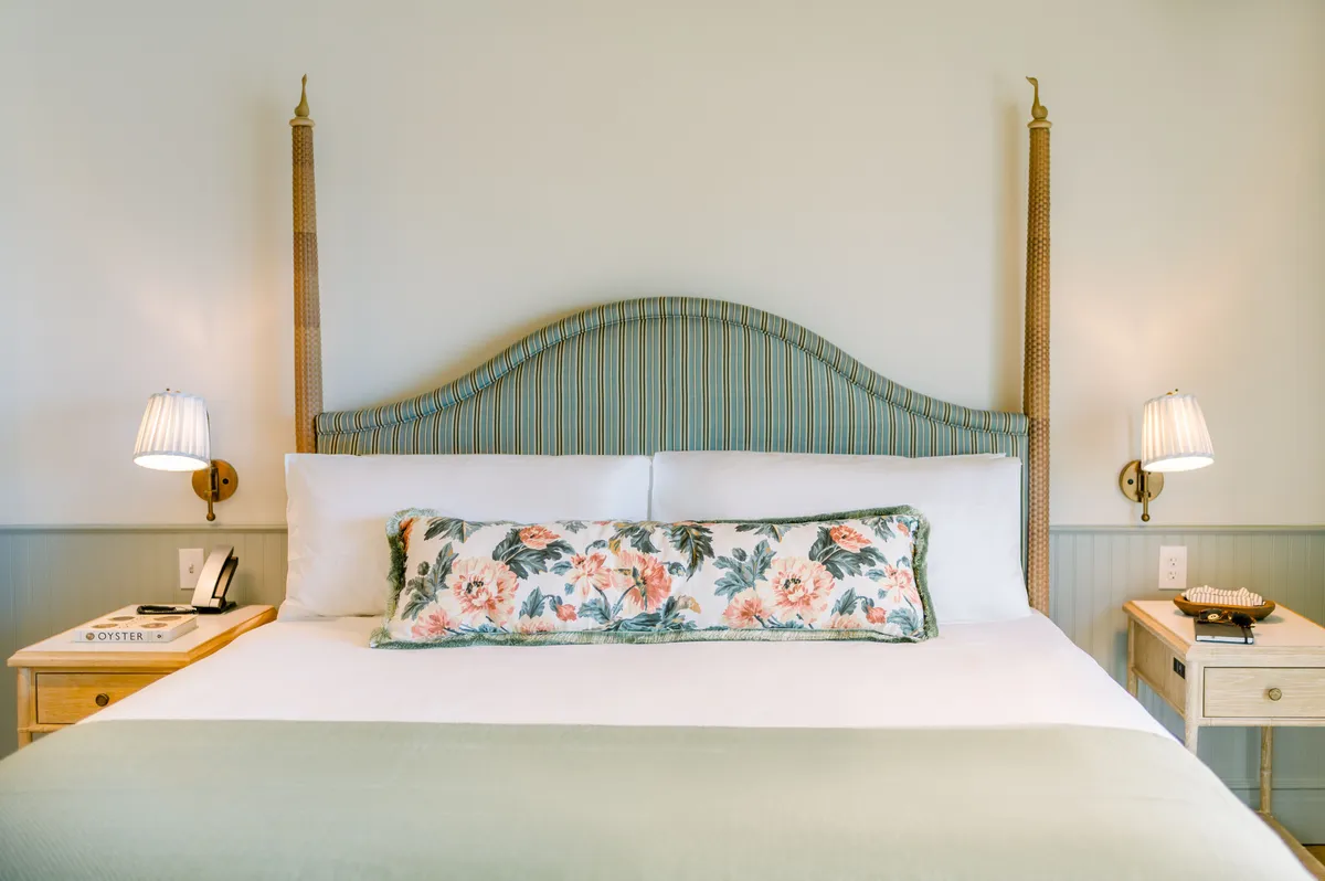 A cozy bedroom scene featuring a decorative headboard, a floral pillow, and a nightstand with a lamp. The soft lighting and inviting bed evoke feelings of comfort and relaxation, suggesting a seamless transition from indoor peace to outdoor bliss on the balcony.