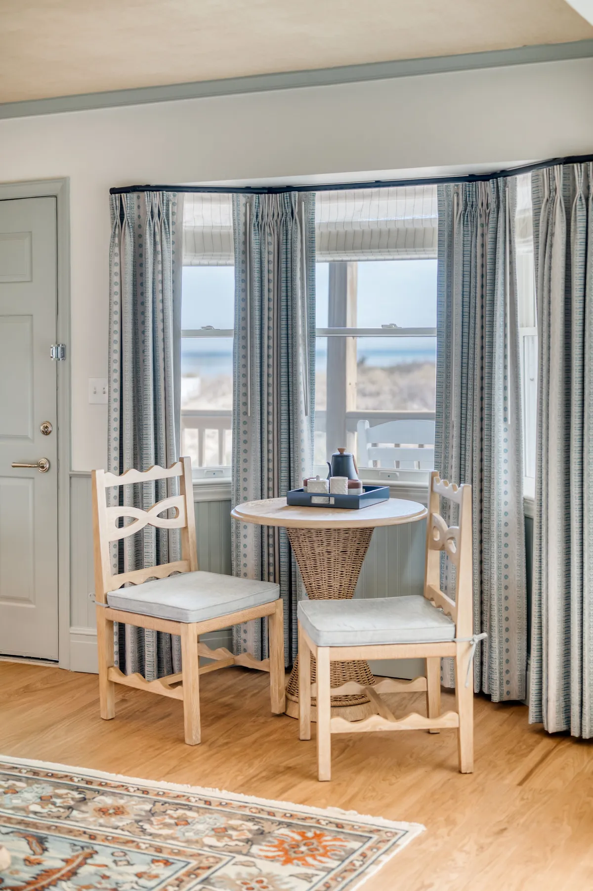 This image shows a cozy wooden table with two chairs positioned near window curtains, creating an intimate dining nook. A decorative tray sits on the table, suggesting readiness for coffee, tea, or a light meal. The soft natural light streaming through the window enhances the sense of warmth and tranquility, ideal for breakfast, games, or planning the day.