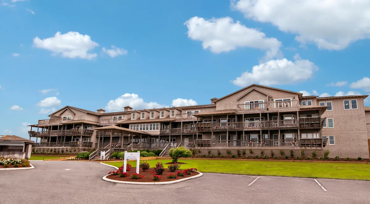The image shows the building’s facade featuring private balconies overlooking a lush, landscaped garden. The balconies are furnished and inviting, with soft evening light hinting at sunset views. The greenery below adds a sense of serenity and privacy to each balcony space.